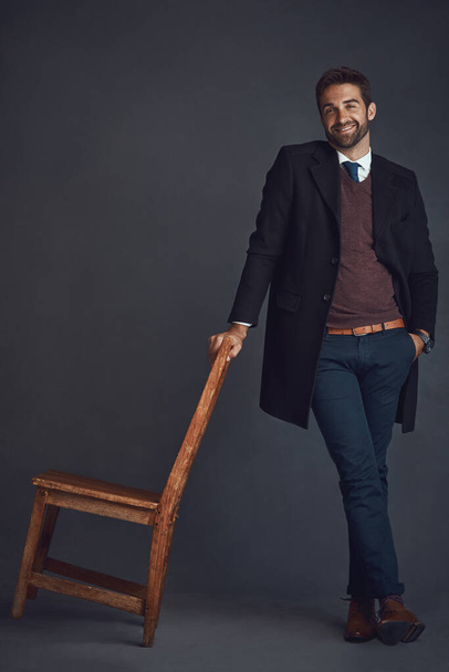 Wear your best and feel your best. Studio portrait of a stylishly dressed young man standing next to a chair against a gray background. - Foto, Imagem