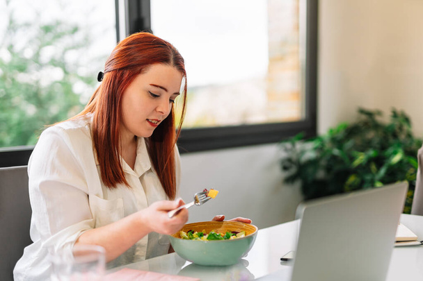 Healthy young woman eating salad while working - Fotó, kép