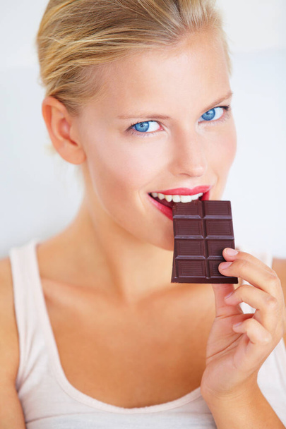 Just a small piece.... Smiling young woman enjoying a delicious piece of chocolate. - Valokuva, kuva
