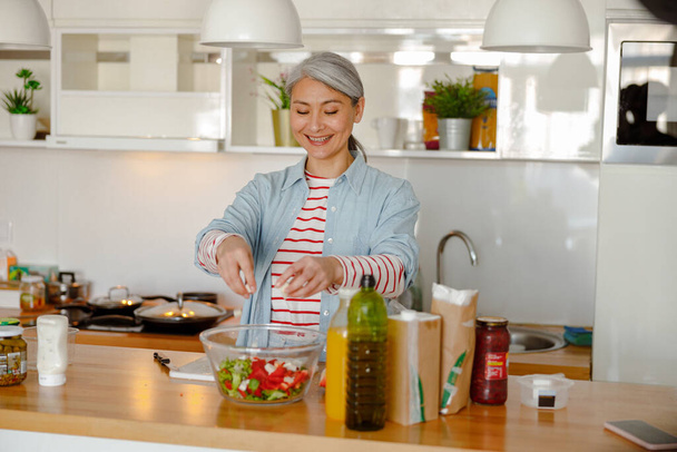 Cheerful woman adding tofu to salad in kitchen - Photo, Image