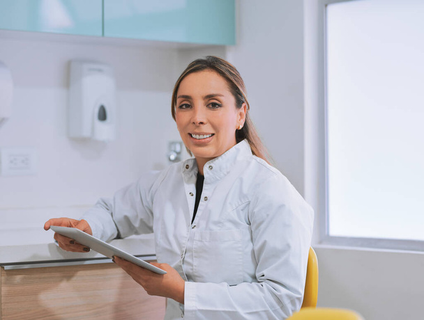 Looking after your oral health. Portrait of a cheerful young female dentist working on her digital tablet while looking at the camera in her office. - Foto, Imagen