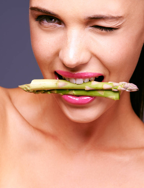 Flirting with food. Portrait of a woman biting on a bunch of asparagus in studio. - Фото, зображення