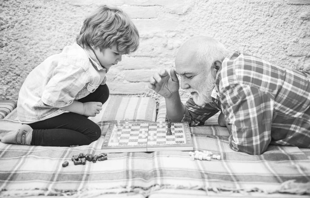 Senior man teaching his grandson to play chess. Handsome grandpa and grandson are playing chess while spending time together at home. - Foto, afbeelding