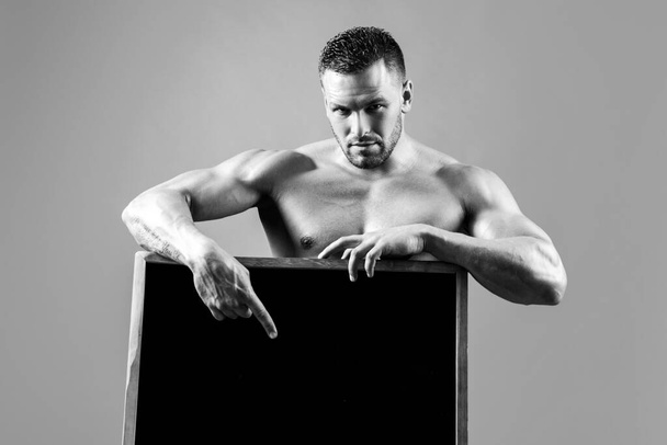 Fitness man with sign ad board. Strong bodybuilder macho holding blank poster isolated on gray background. - Фото, изображение