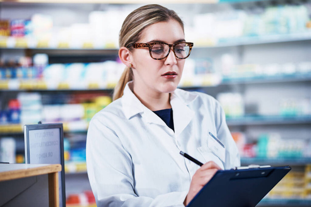 Taking notes of all the medical stock in store. Shot of a young pharmacist writing on a clipboard in a pharmacy. - Photo, Image