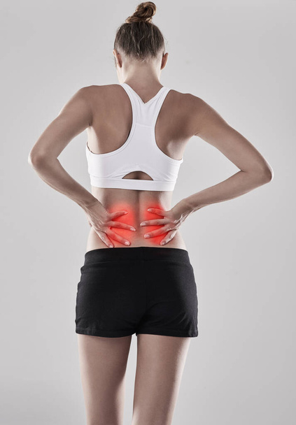 Rückenschmerzen können wirklich unerträglich und unangenehm sein. Schuss einer jungen Frau, die ihren verletzten Rücken hält, der rot hervorgehoben ist. - Foto, Bild