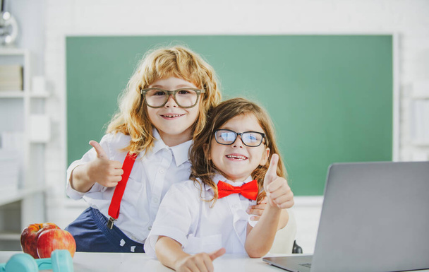 School friends. Two school kids, cute girl and boy with thumbs up at school near blackboard. - Фото, зображення