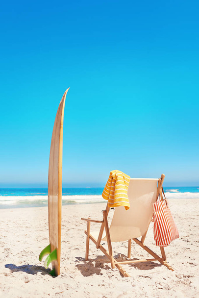 Ready for the waves. Shot of a lounge chair and a surfboard on the beach. - Photo, Image