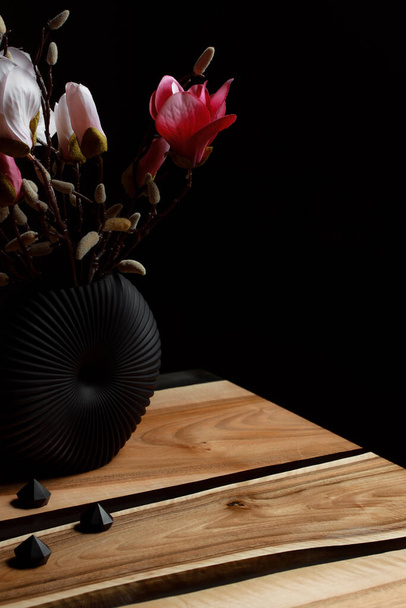 Ακριβά παλιά έπιπλα. Το τραπέζι είναι καλυμμένο με εποξειδική ρητίνη και γυαλισμένο. Πολυτελής επεξεργασία ξύλου ποιότητας. Ένα μπουκέτο από κόκκινα και ροζ λουλούδια σε μια μινιμαλιστική μαύρη γλάστρα. - Φωτογραφία, εικόνα