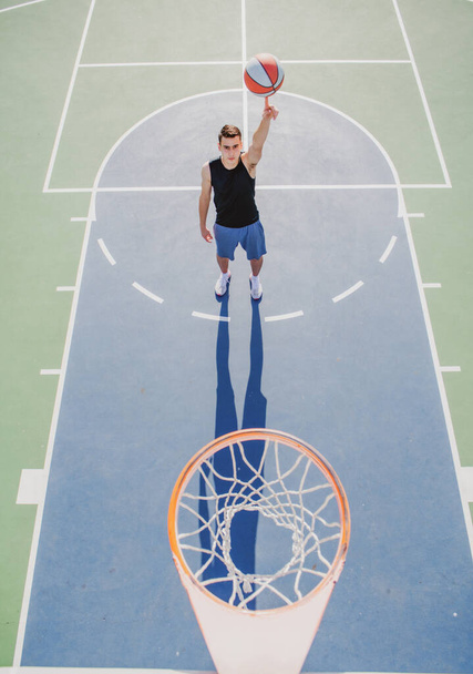 Angle view of man playing basketball, above hoop of man shooting basketball. Hand spinning basket ball. Balancing basketball on finger. - Foto, afbeelding
