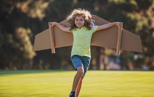 Kids fly. Funny child boy pilot flying with toy cardboard airplane wings in park, copy space. Start up freedom concept, carefree kid. - Foto, imagen