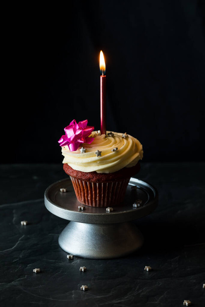 Un cupcake di velluto rosso con glassa di crema di formaggio condita con spruzzi e un fiocco - Foto, immagini