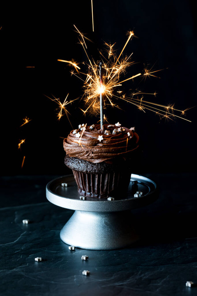 A chocolate cupcake topped with chocolate icing, sprinkles and a lit sparkler. - 写真・画像