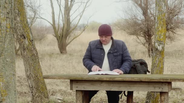człowiek w naturze, czyta książkę siedzącą przy drewnianym stole - Materiał filmowy, wideo