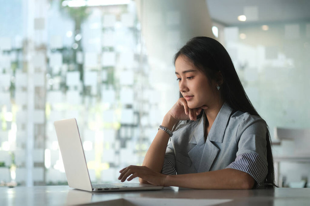 Молодая деловая женщина, сидящая в светлом современном офисе и используя ноутбук. - Фото, изображение