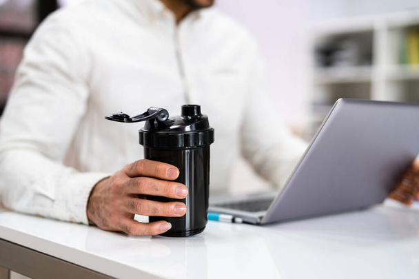 Protein Shake On Desk And Man In Foreground Using Computer - Foto, Bild