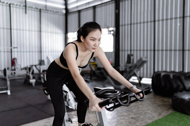 Концепция упражнений Спортивная женщина с серьезным лицом езда на велосипеде упражнения машина в одиночку в середине тренажерного зала. - Фото, изображение