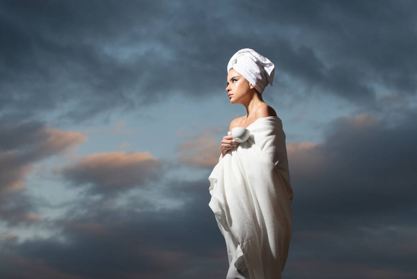Relaxed woman in bathrobe with towel on head smelling coffee in the night at dramatic sky outdoor. Morning spa. - Fotoğraf, Görsel
