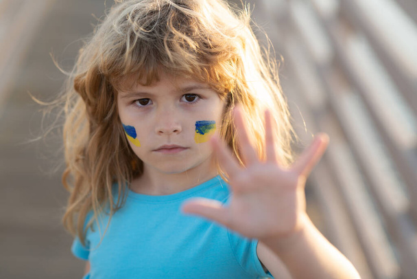 Ukraine flag on kids cheek. Little ukrainian patriot. Stop the war hand gestures. No war, stop war, russian aggression. Human protest. - Foto, Imagem