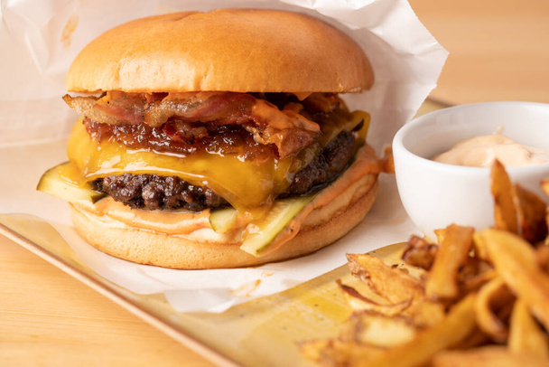 zblízka šťavnatý čerstvý cheeseburger s hranolky a omáčkou, na dřevěném stole - Fotografie, Obrázek