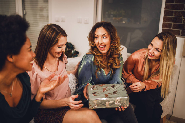 Cheerful multiethnic girls giving presents to each other while gathering at home to celebrate Christmas or New Year. - Foto, Bild