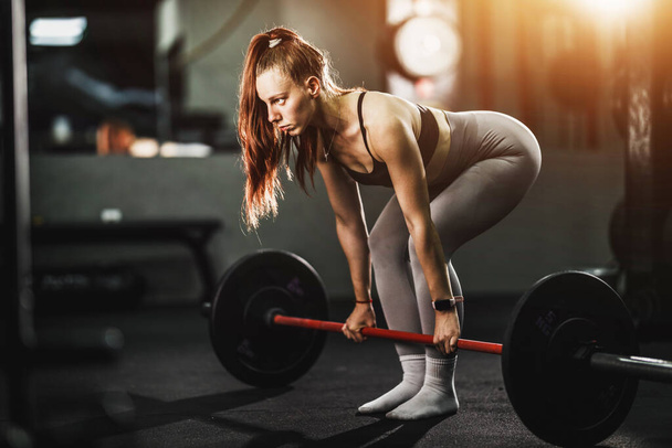 Shot of a muscular young woman doing deadlift exercise with barbel in the gym. - Zdjęcie, obraz
