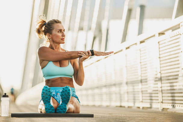 Middle age sports woman warming up and stretching her arms on a bridge. - Foto, Imagem