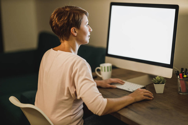 Femme pigiste d'âge moyen travaillant tard sur ordinateur dans son bureau à domicile pendant la quarantaine pandémique. - Photo, image
