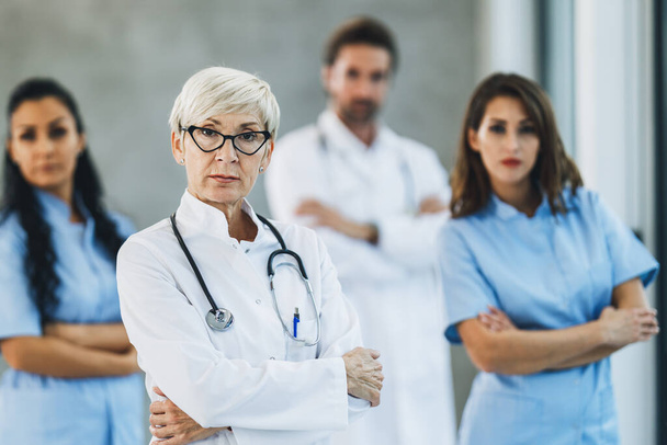 Portrait d'une femme médecin confiante debout les bras croisés dans un couloir d'hôpital avec ses collègues en arrière-plan. - Photo, image