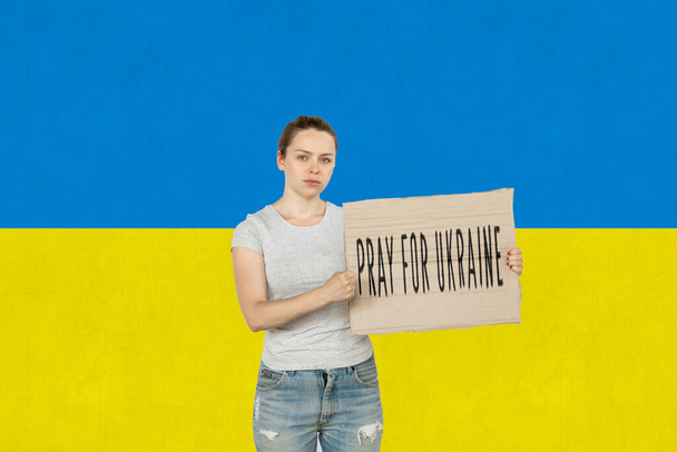 Conceptual image. Young girl holding tablet with lettering Pray for Ukraine isolated over ukrainian blue and yellow flag background - Zdjęcie, obraz