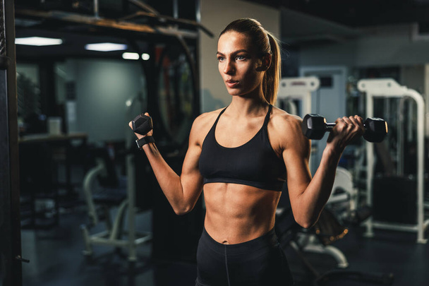 Una giovane donna muscolosa sta facendo allenamento con i manubri per il muscolo bicipite in palestra. - Foto, immagini