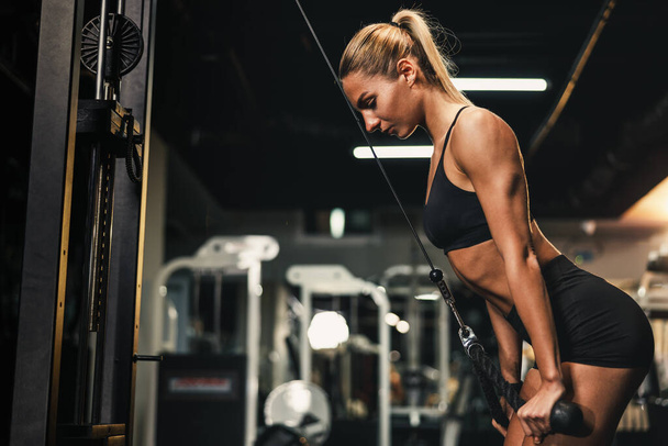 Una joven musculosa está entrenando en la máquina para el músculo de sus brazos en el gimnasio. - Foto, imagen
