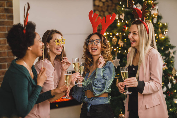 Fröhliche multiethnische Mädchen haben Spaß beim gemeinsamen Anstoßen mit Champagner auf Weihnachten oder Neujahr. - Foto, Bild