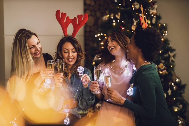Wesołe wielonarodowe koleżanki bawią się podczas toastu z szampanem na Boże Narodzenie lub Sylwestra. - Zdjęcie, obraz