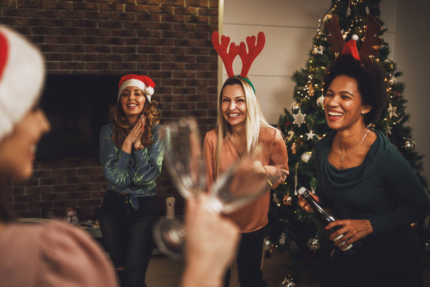 Amici femminili multietnici allegri che si divertono e fanno un brindisi con champagne mentre festeggiano l'Anno nuovo o il Natale a casa insieme. - Foto, immagini