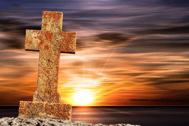 Close-up de uma velha pedra Cruz religiosa contra um belo pôr do sol com raios de sol no horizonte acima do mar. - Foto, Imagem