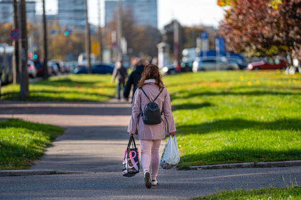 Riga, Lotyšsko, 9. října 2021: žena s nákupními taškami na chodníku, zadní pohled, rozmazané městské pozadí - Fotografie, Obrázek
