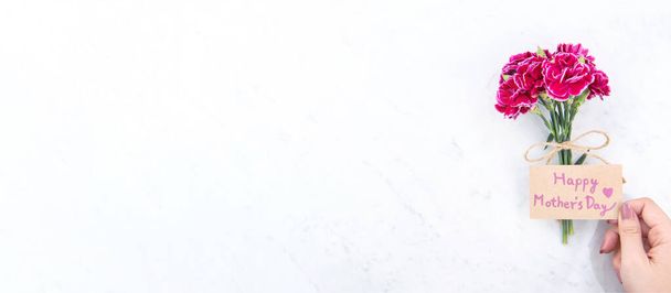 Mayo madres idea del día concepto de fotografía - Hermosos claveles en flor atados por la cuerda kraft arco sosteniendo en la mano de la mujer aislado en la mesa moderna brillante, espacio de copia, posición plana, vista superior - Foto, imagen
