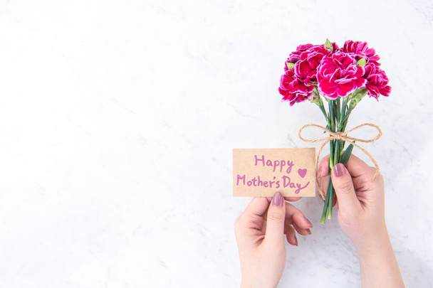 May mothers day idea concept photography - Beautiful blooming carnations tied by rope kraft bow holding in woman's hand isolated on bright modern table, copy space, flat lay, top view - Foto, afbeelding