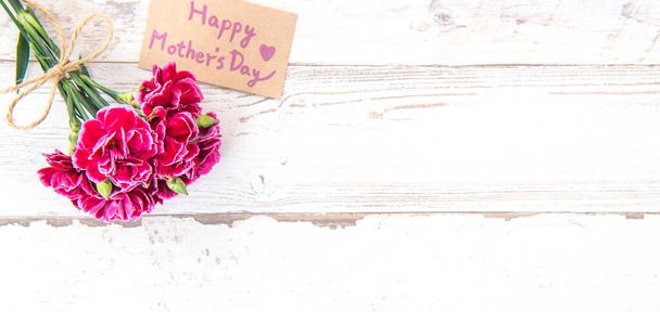 May mothers day concept photography - Beautiful carnations with template card isolated on a bright wooden table, copy space, flat lay, top view, mock up - Foto, afbeelding
