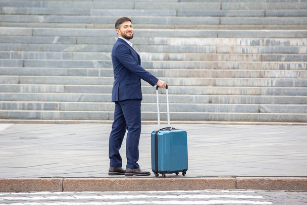 Successful businessman with travel suitcase at city street crossing - Фото, зображення