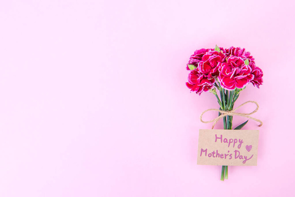 May mothers day idea concept photography - Beautiful blooming carnations tied by bow with kraft text card isolated on bright modern table, copy space, flat lay, top view - Φωτογραφία, εικόνα