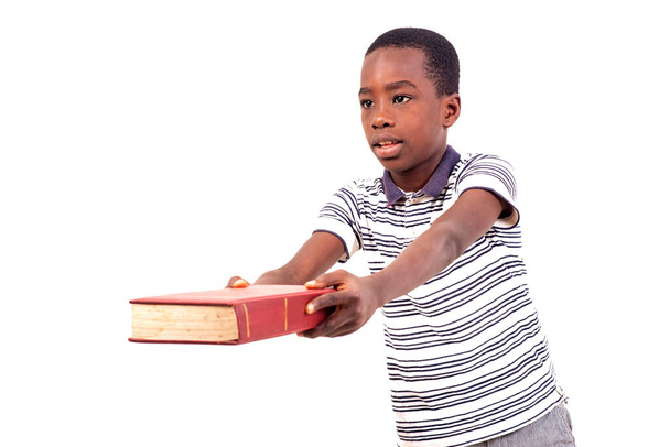 kleiner Junge im T-Shirt steht auf weißem Hintergrund und gibt jemandem ein Buch. - Foto, Bild