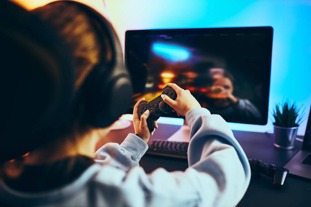 自宅でビデオゲームをしている10代の少女。ゲーマーは、画面の前に座ってゲームパッドを保持。ネオンライトで照らされた暗い部屋でオンラインで遊ぶストリーマー。競争と楽しみ - 写真・画像