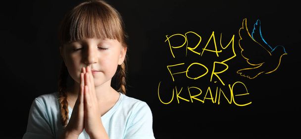 Uskonnollinen pieni tyttö ja teksti PRAY for UKRAINE on dark background - Valokuva, kuva