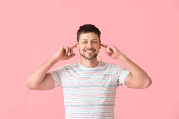 Handsome man putting ear plugs on pink background - Photo, Image