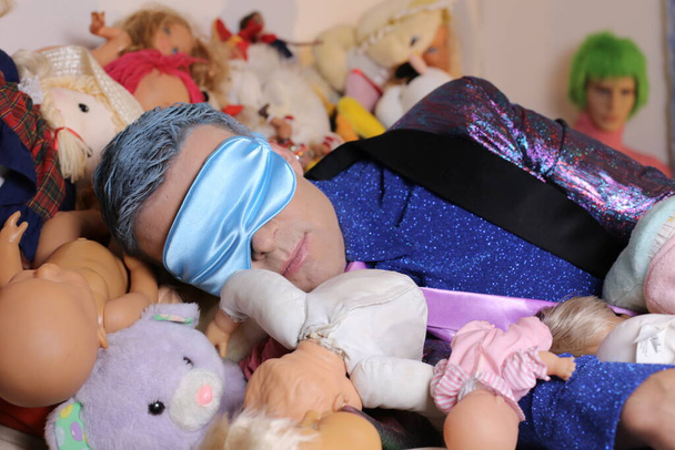 close-up portrait of handsome young man in suit in bed full of soft toys - Photo, Image