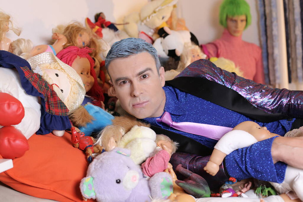 close-up portrait of handsome young man in suit in bed full of soft toys - Photo, Image