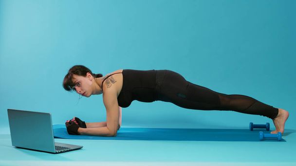 Athete zitten in plank positie op yoga mat over blauwe achtergrond - Foto, afbeelding
