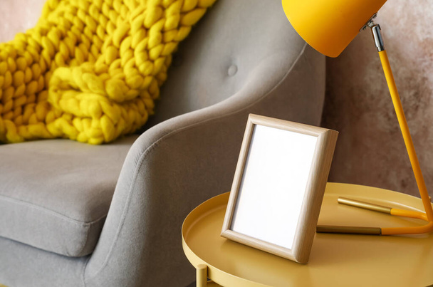 Stylish coffee table with lamp, frame and comfortable armchair near color wall, closeup - Фото, зображення